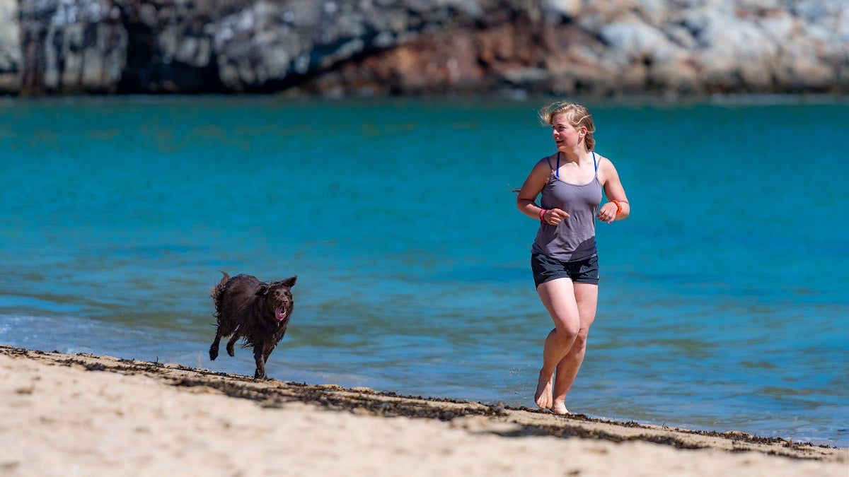 Woman running with a black dog by the beach
