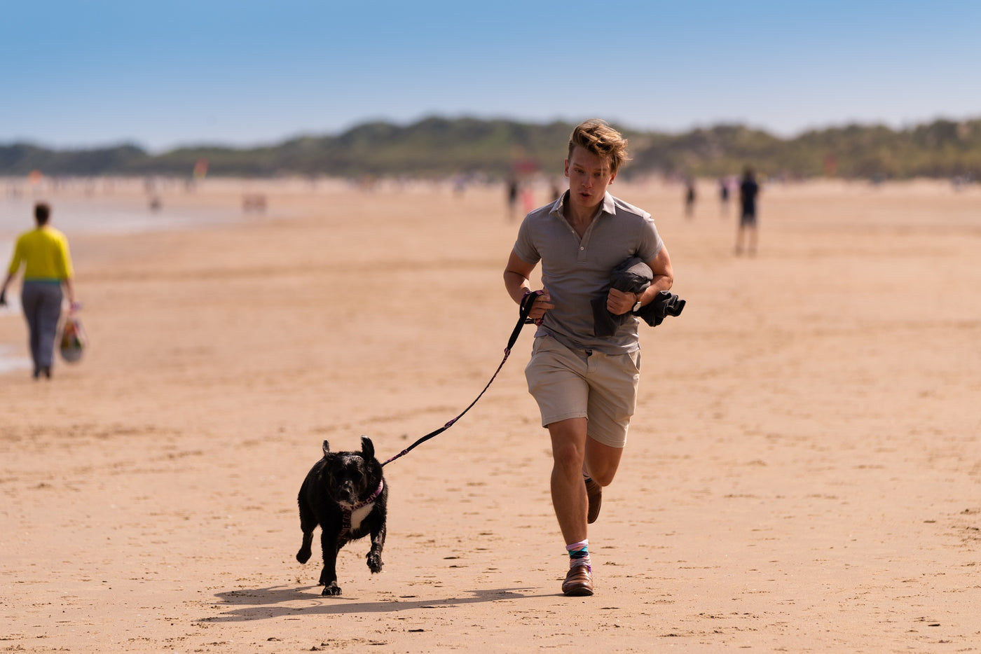 man running with dog wearing a leash on the beach